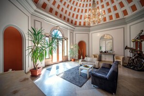 A spacious living room with a high ceiling, a chandelier, a large potted plant, a sofa, a coffee table, and a motorcycle. - Accessible Double Room (Schlitz)