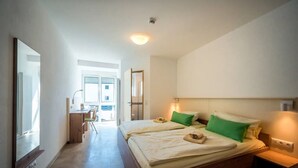 Un dormitori modern amb un llit gran, un escriptori i una cadira, un bany amb dutxa, i vistes a l'exterior.