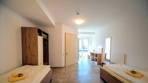 A bedroom with two beds, a wooden wardrobe, a desk with a chair, and a door leading to a balcony. - Accessible Double Room (Schlitz)