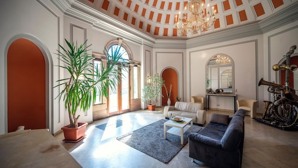 A spacious living room with a high ceiling, a chandelier, a large potted plant, a sofa, a coffee table, and a motorcycle. - Accessible Double Room (Schlitz)