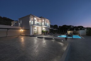 Ein modernes, zweistöckiges Haus mit Schwimmbad, Sitzgelegenheiten im Freien und Topfpflanzen.