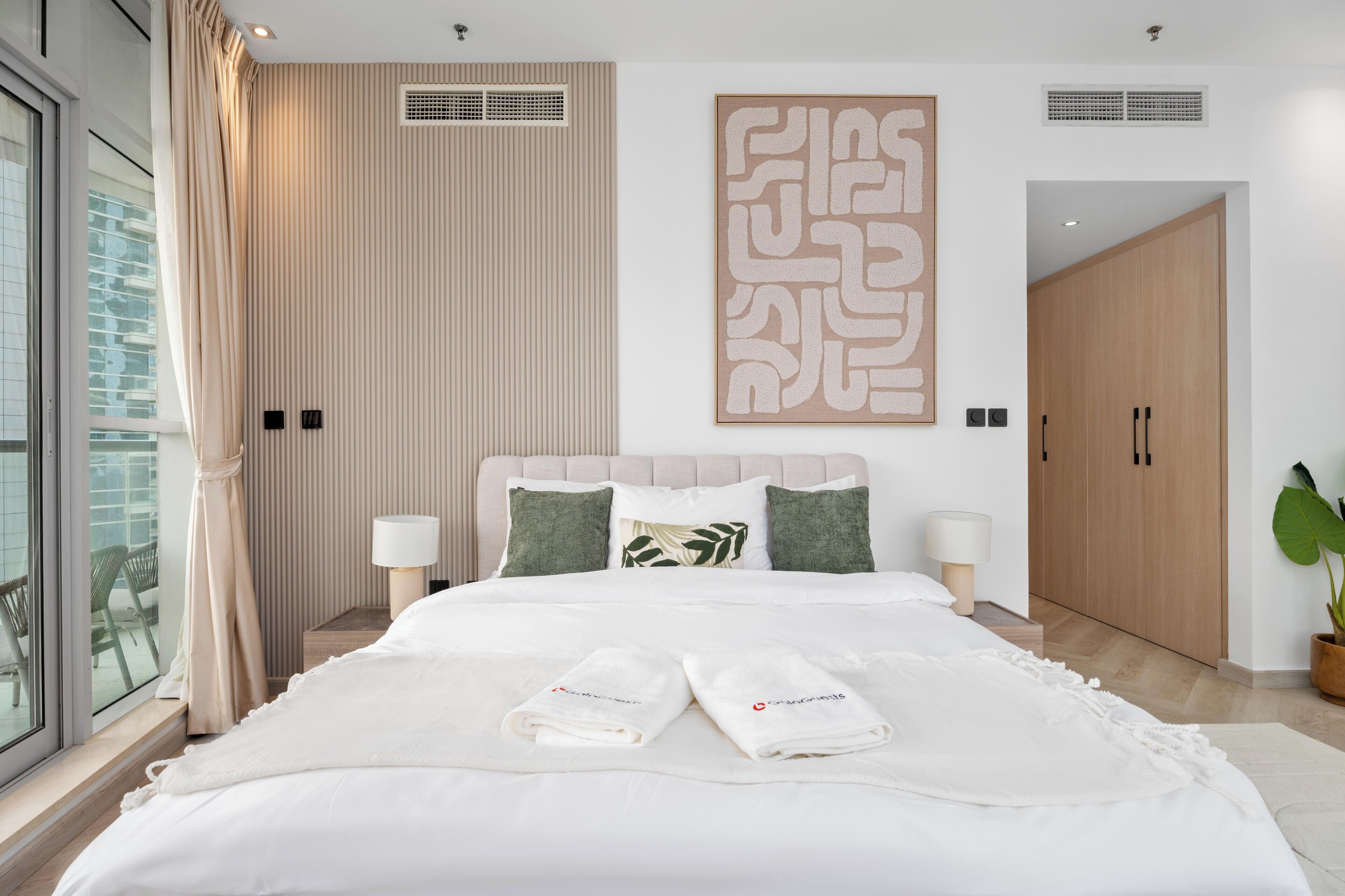 A modern hotel room with a large bed, two bedside tables, a large window, and a view of the outside.