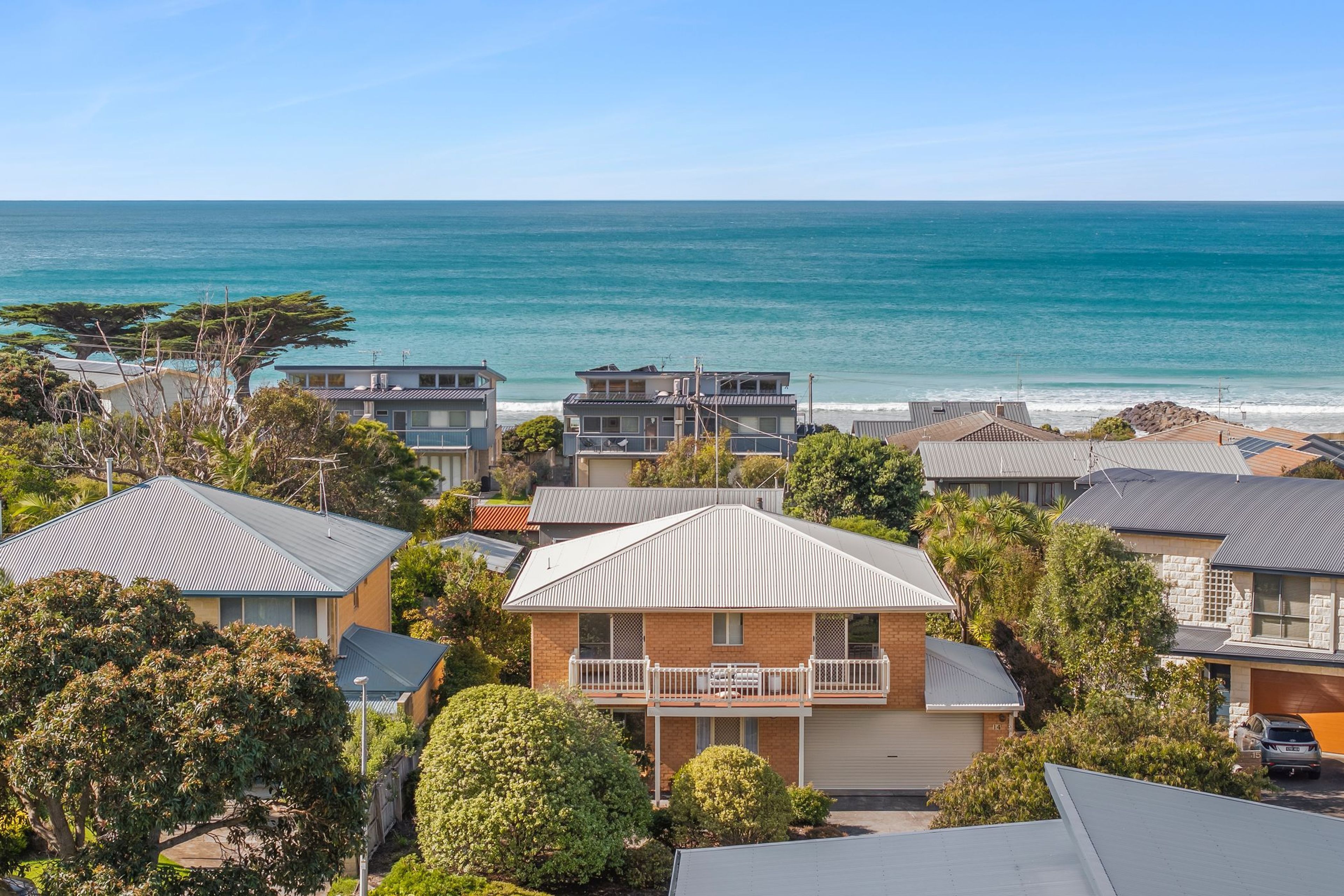 A coastal residential area with houses, a clear view of the ocean, and a variety of vegetation.