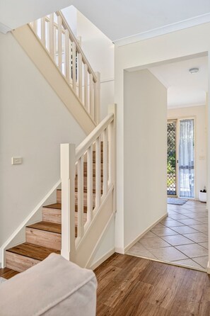 A staircase with wooden steps and white railings leading to a room with a large window and a view of the outdoors. - The Happy Bay House (Apollo Bay)