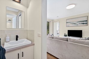 A modern bathroom with a large mirror, a white sink, and a shower area. - The Happy Bay House (Apollo Bay)