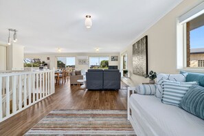 A spacious living area with a sofa, a dining table, and a kitchen in the background. - The Happy Bay House (Apollo Bay)