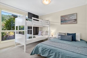 A bedroom with bunk beds, a single bed, a nightstand, a lamp, and a painting on the wall. - The Happy Bay House (Apollo Bay)