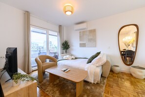 A hotel room with a bed, a desk, a chair, a television, a window with a view, and a mirror. - M (MOS34D7E) Spacious and elegant two-bedroom apartment with terrace (Madrid)