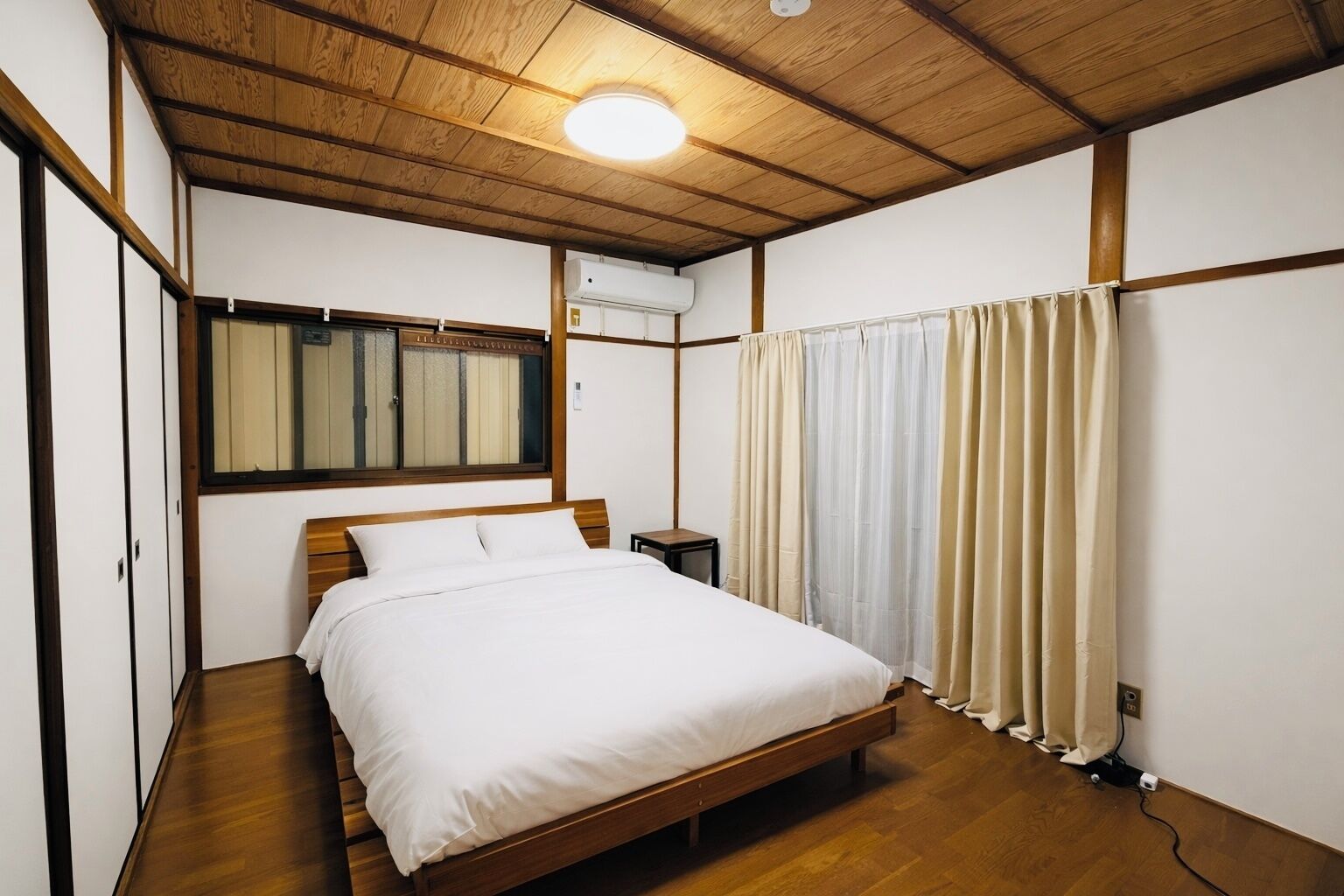 Une chambre à coucher avec un lit en bois, une table de chevet, une fenêtre avec des rideaux et un appareil de climatisation.