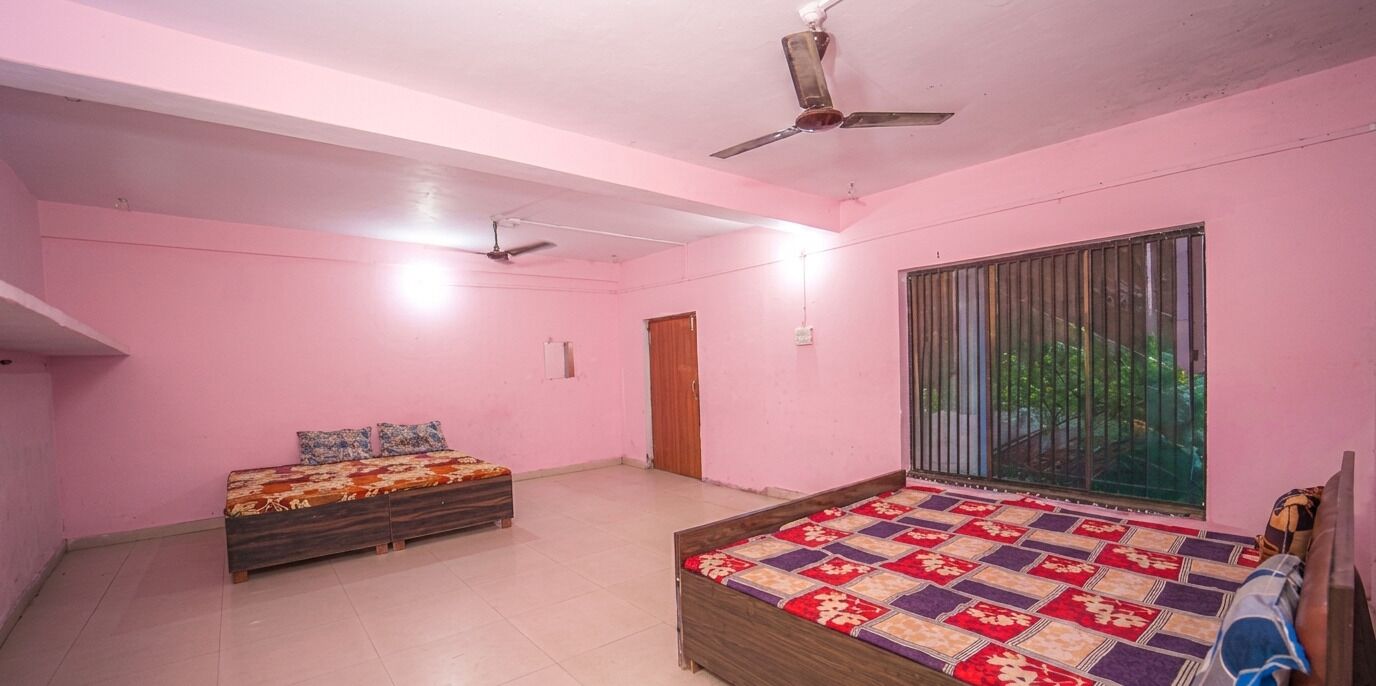 A pink-walled bedroom with two beds, a ceiling fan, and a window with a view.