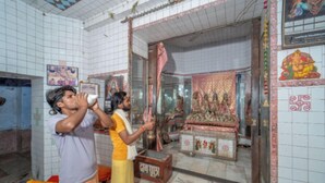 Una habitación con paredes de baldosas, una cama con una colcha roja y un pequeño santuario con objetos religiosos.