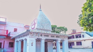 Un pequeño templo con tejado de tejas y aguja, rodeado de edificios.