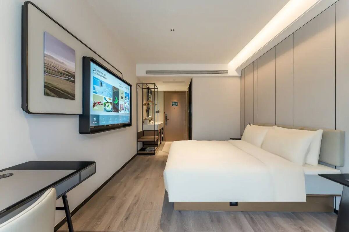 Una habitación de hotel moderna con cama, escritorio, televisor montado en la pared y vista al pasillo.