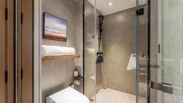 Un baño moderno con cabina de ducha de vidrio, un inodoro, un perchero y una estantería con un cuadro.