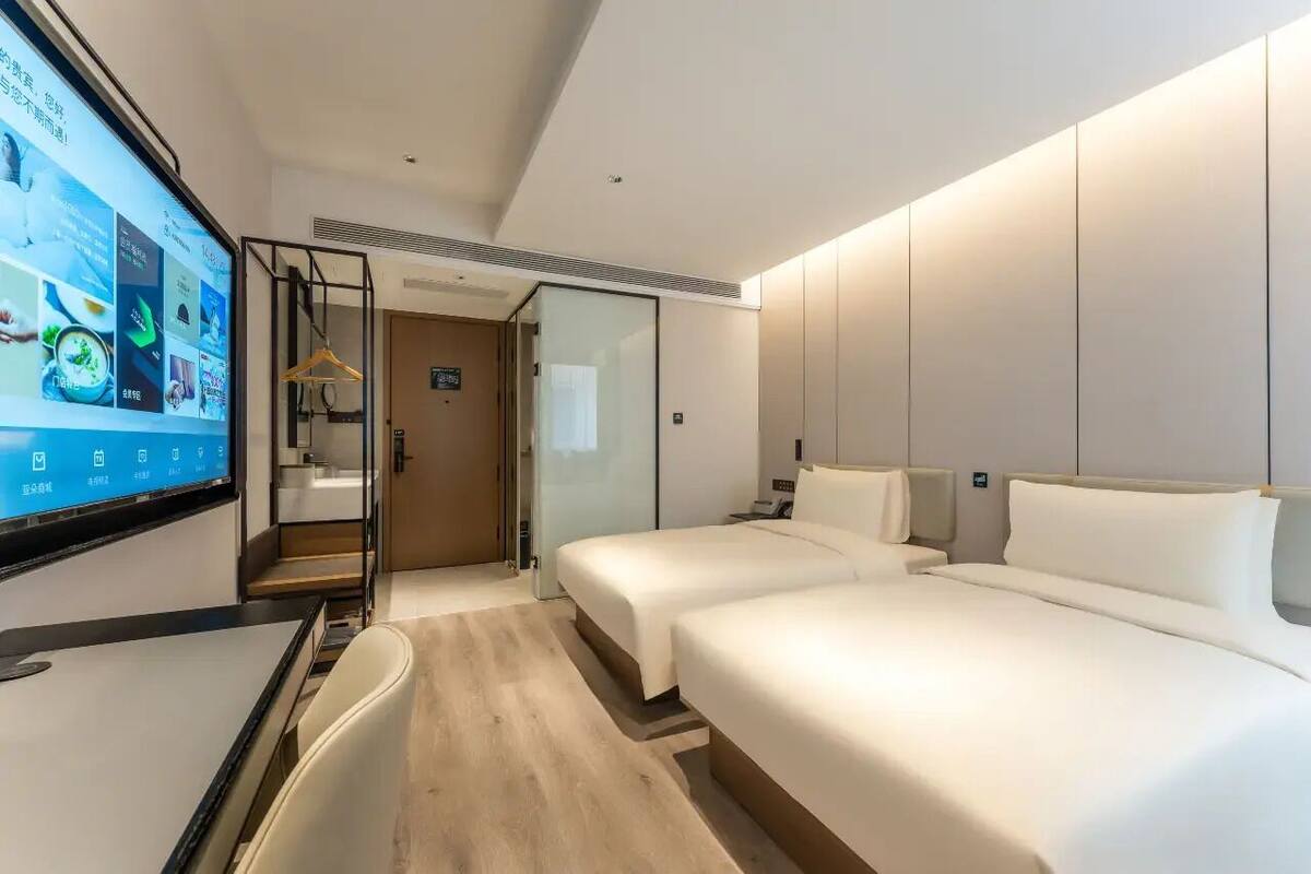 Habitación de hotel con cama, escritorio, televisor y puerta corredera.