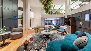 Un moderno vestíbulo de hotel con una zona de estar central, un techo alto y vista al espacio interior.