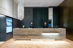 A reception desk with a marble top, a large chandelier, and a digital screen displaying information.