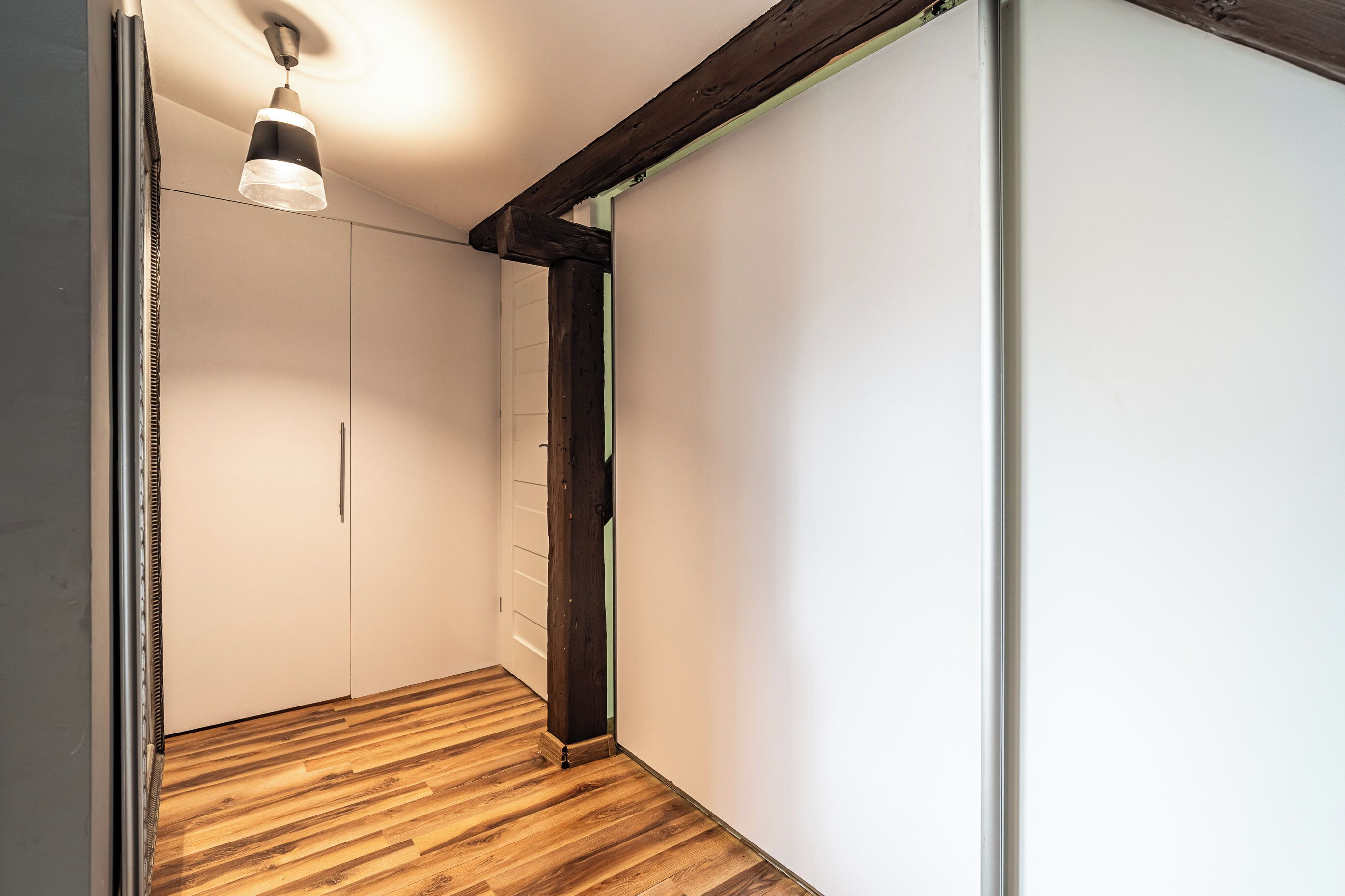 A hallway with wooden flooring, white walls, and a ceiling light fixture.