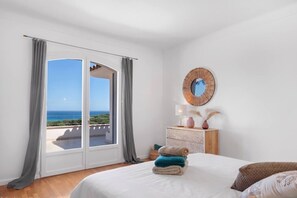 Ein Schlafzimmer mit einem großen Bett, einem Nachttisch, einem Spiegel und Meerblick durch eine Schiebetür.