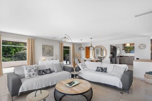 Ein modernes Wohnzimmer mit zwei Sofas, einem Couchtisch und einem Essbereich, im Hintergrund ist eine Küche erkennbar.