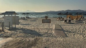 A beach with a wooden boardwalk, beach chairs, umbrellas, and a sign welcoming to Marmari. - Evita Flamingo (Kos)