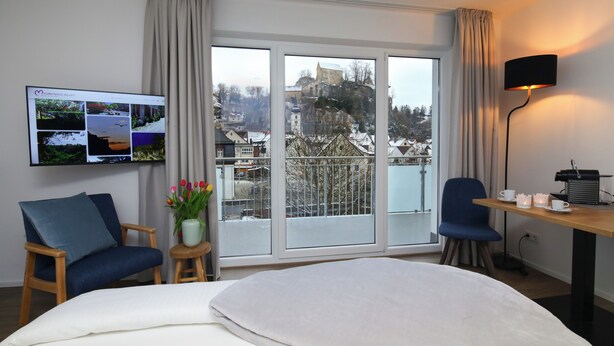Habitación de hotel con una cama grande, un escritorio con lámpara, un televisor mostrando imágenes y vista a un paisaje nevado por la ventana.