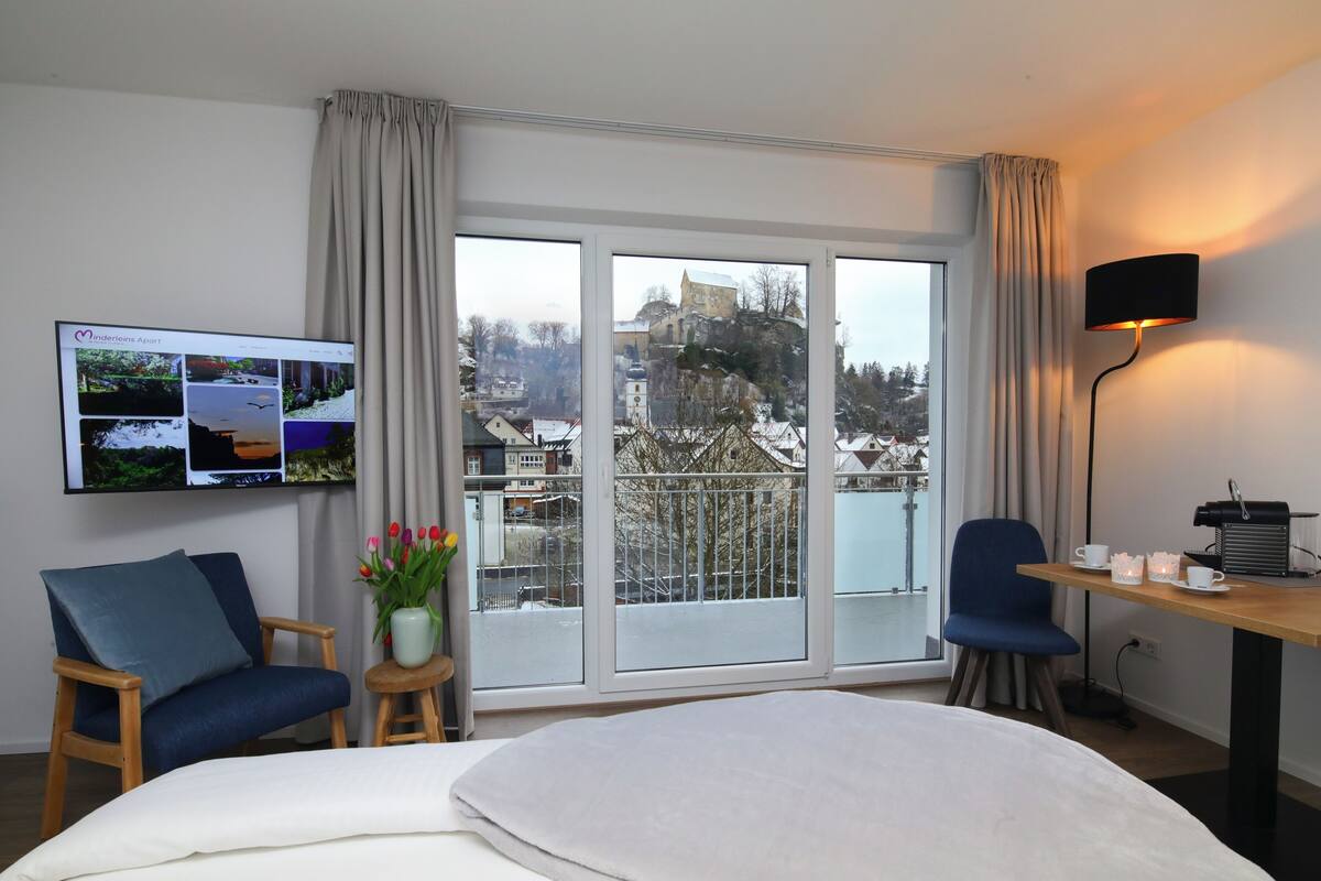 Habitación de hotel con una cama grande, un escritorio con lámpara, un televisor mostrando imágenes y vista a un paisaje nevado por la ventana.