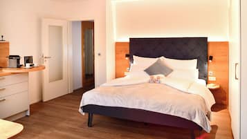 A modern hotel room with a bed, bedside tables, a desk, and a door leading to another room.