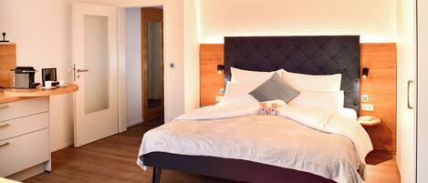 A modern hotel room with a bed, bedside tables, a desk, and a door leading to another room.
