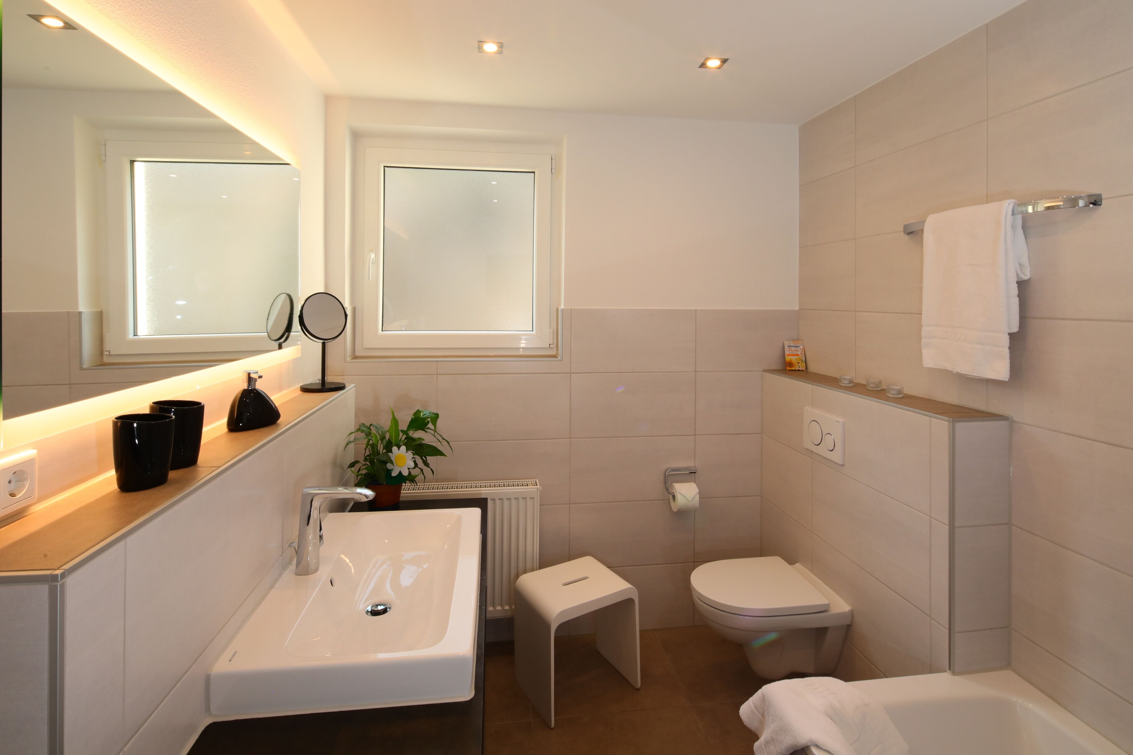 Une salle de bain moderne équipée d’un lavabo, d’un miroir, de toilettes et d’une baignoire.