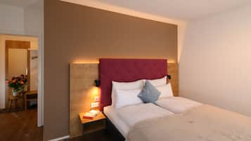 Un dormitorio con cabecera de madera, una mesita de noche con lámpara, cama con ropa de cama blanca y una pequeña mesa con un florero.