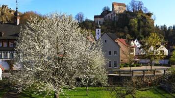 A town with a prominent white tree in the foreground, a church with a bell tower, and a castle on a hill in the background.