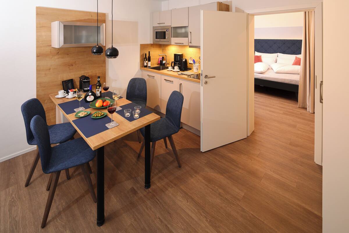 Habitación de hotel pequeña con comedor, kitchenette y cama.