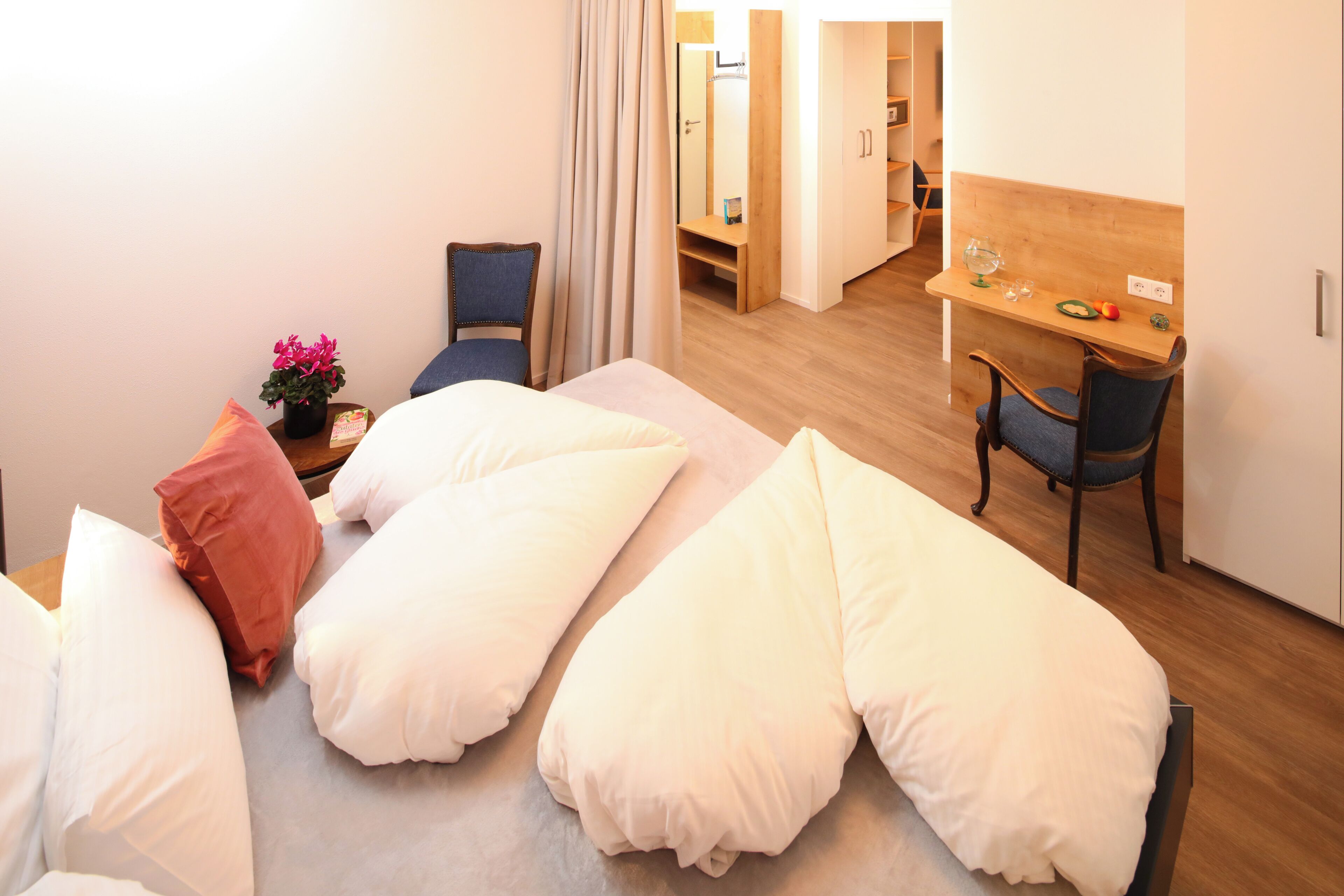 A hotel room with a bed, a desk, a chair, and a small table with a plant.