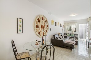 A modern living room with a glass dining table, a sofa, and a large abstract wall art piece.