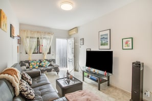 A living room with a sofa, ottoman, TV, and a tall black speaker. - Vacation Home 'Casa Klemann Private Sun Terrace' with Mountain View, Wi-Fi and Air Conditioning (Cruce de Arinaga)