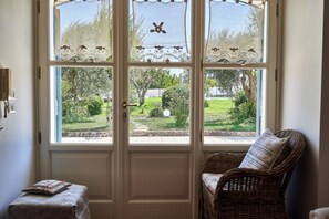 Ein Zimmer mit einem Korbstuhl, einem kleinen Tisch mit Kissen und einer Tür, die in einen Garten führt.