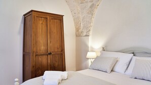 Een slaapkamer met een bed, kussens, een houten garderobe en een lamp.