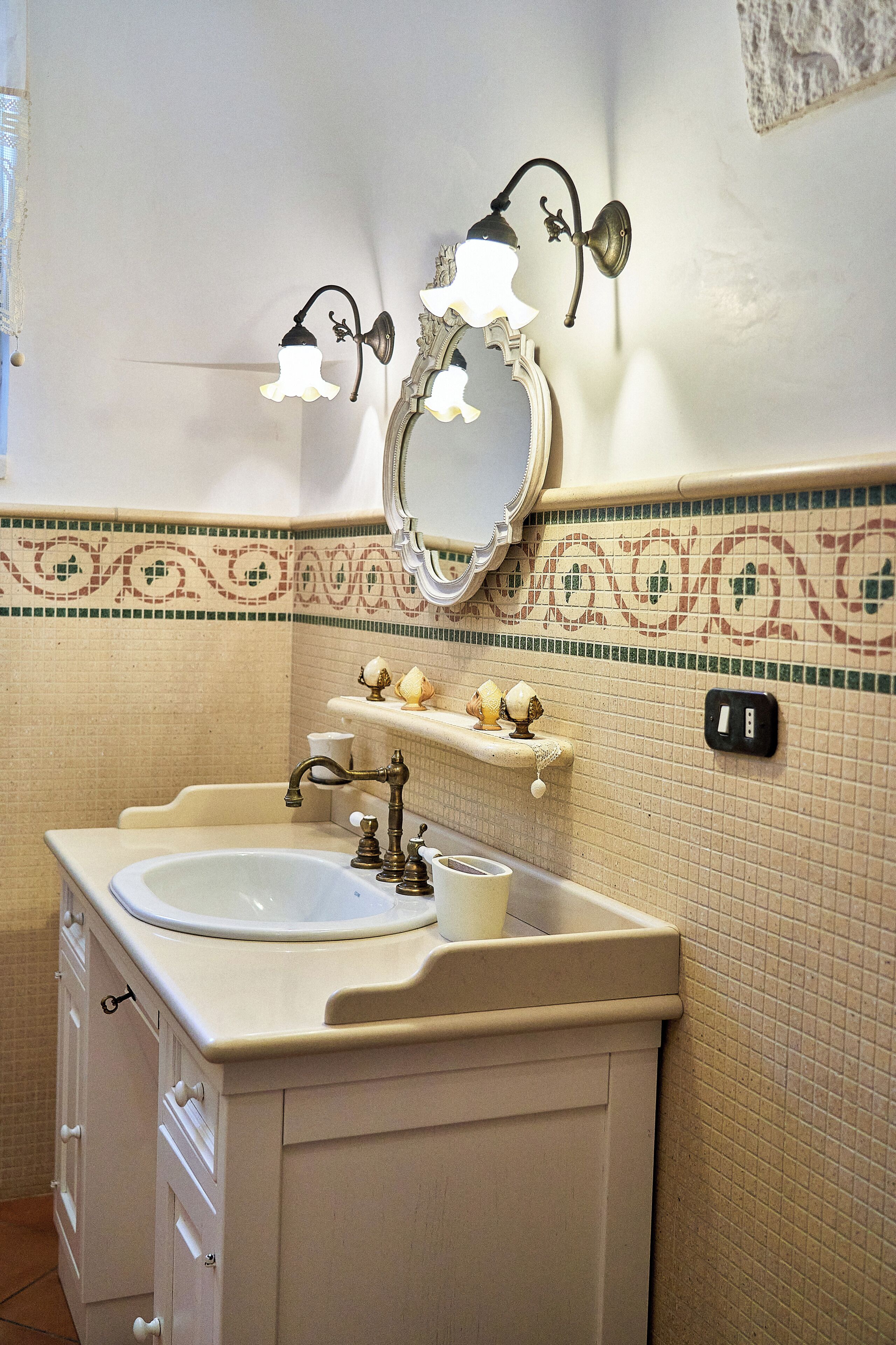 A bathroom with a sink, mirror, wall-mounted lights, and decorative tiles.