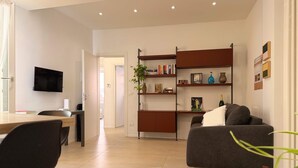 Ein modernes Wohnzimmer mit einer Couch, einem an der Wand montierten Fernseher, einem Bücherregal und einem Essbereich mit Stühlen.