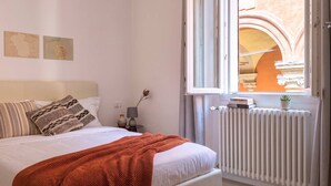 Ein Schlafzimmer mit Bett, Fenster, Heizkörper und Blick auf ein Gewölbe.