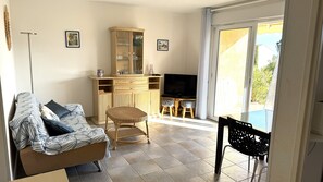 A living room with a sofa, a TV, a cabinet, and a dining area with chairs. - Apartment "Bord de Mer" 5min beach, pool, AC (Fréjus)