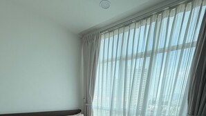 Et moderne hotelværelse med en stor seng, udsigt over byen gennem lette gardiner, og en balkon.