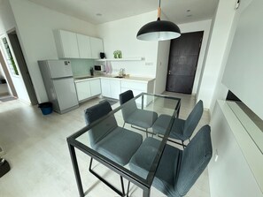 Eine moderne Küche mit weißen Schränken, einem schwarzen Kühlschrank und einem Glastisch mit vier Stühlen.