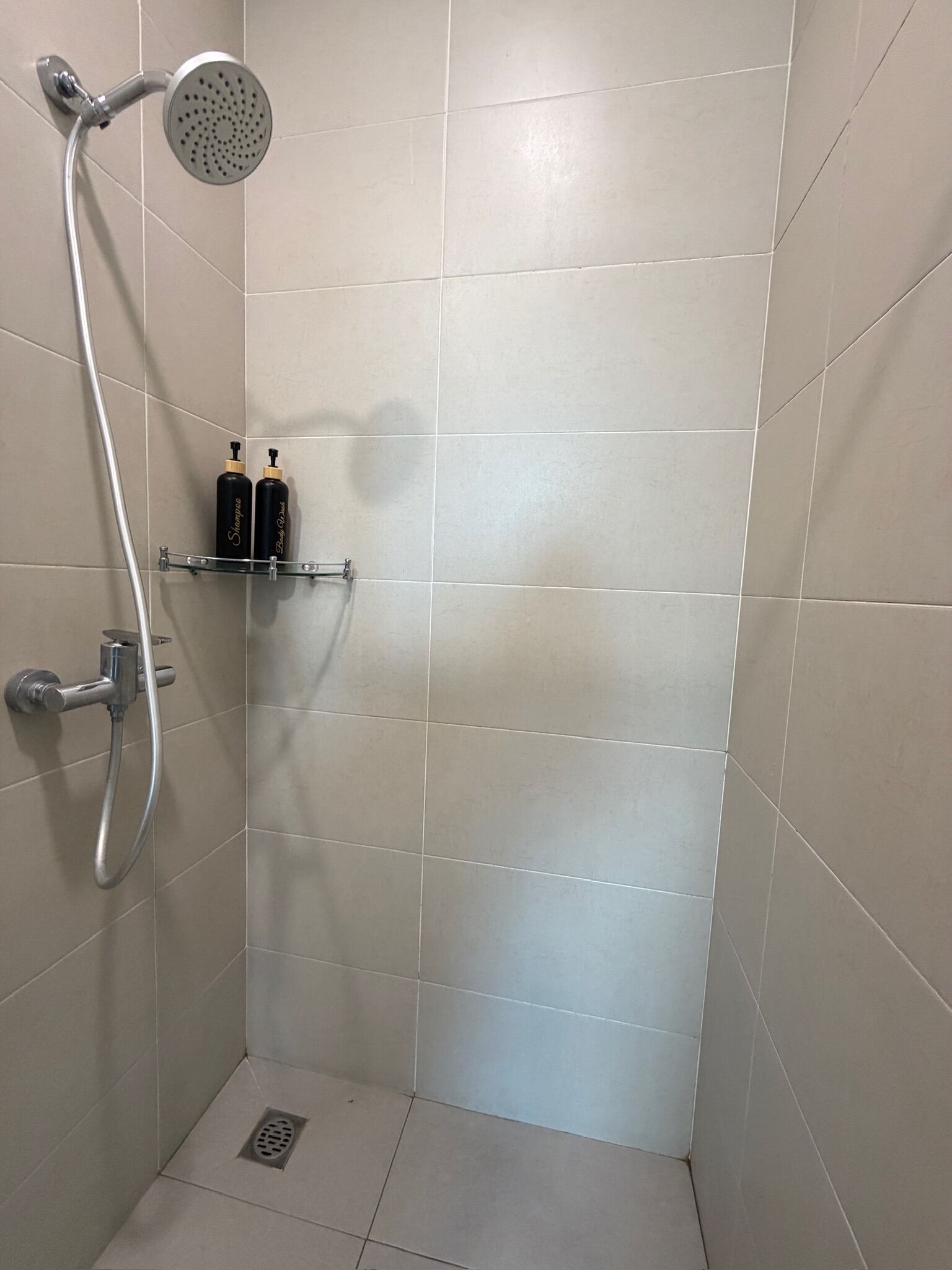 A shower with a handheld showerhead, a wall-mounted faucet, and a shelf with two bottles.