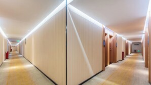 A long, narrow hotel corridor with wooden panel walls, a carpeted floor, and a ceiling with recessed lighting.