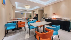 A modern dining area with tables and chairs, a counter with food display, and a chandelier.