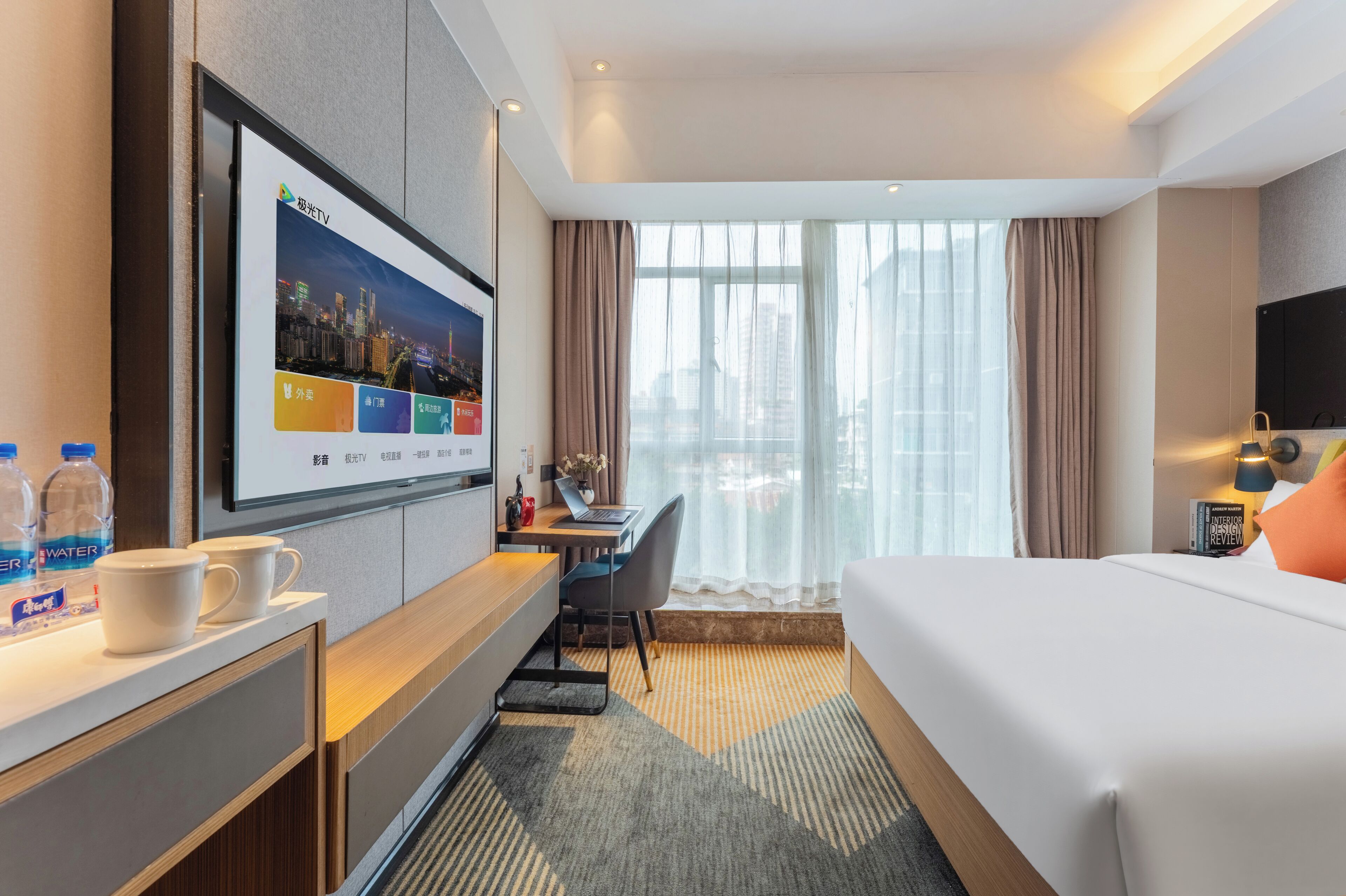 A hotel room with a bed, desk, TV, and a view of the city.
