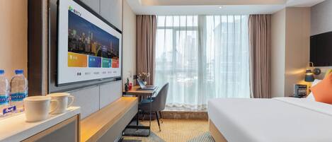 A hotel room with a bed, desk, TV, and a view of the city.