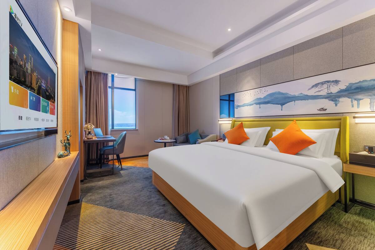 Quarto de hotel com uma cama grande, uma escrivaninha com um laptop, uma mesinha e uma TV fixada na parede.